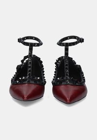 Bailarinas de piel roja con punta afilada, que cuentan con correas de tachuelas negras y detalle en el tobillo para mayor soporte.