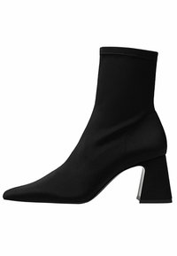 Bottine noire à bout pointu, supérieure en textile extensible et talon chunky avec un accent métallique. Texture lisse dans l'ensemble.