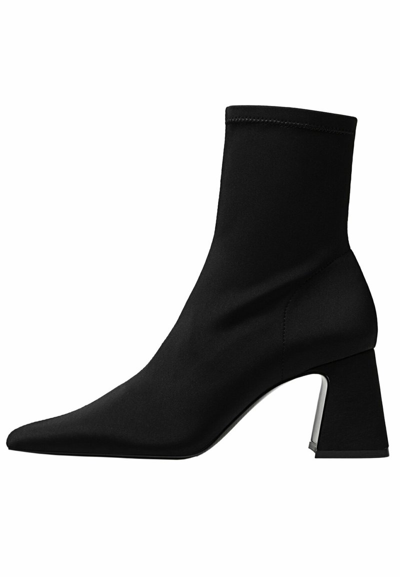Bottine noire à bout pointu, supérieure en textile extensible et talon chunky avec un accent métallique. Texture lisse dans l'ensemble.