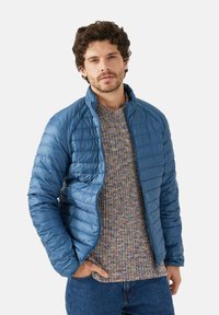 Giacca imbottita blu con design trapuntato leggero e collo rialzato, abbinata a un maglione multicolore in maglia e denim scuro.