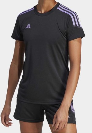 Person wearing a black athletic shirt and shorts with purple stripes on shoulders and sides, standing with arms relaxed by their sides.