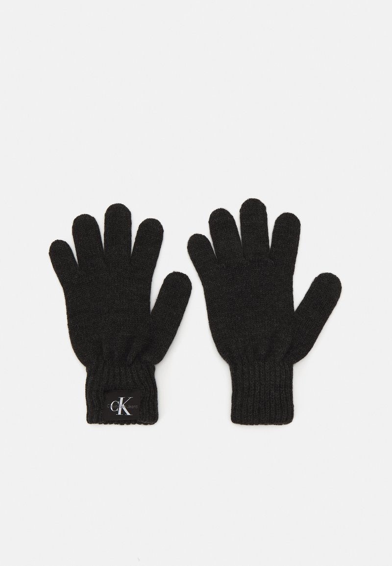 Melnas adītas cimdi ar ribotām piedurknēm un nelielu logo uzšuvumu. Materiāls izskatās teksturēts un nedaudz pūkains. Piecu pirkstu dizains.