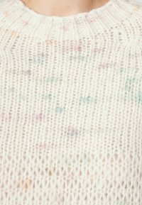 Gros plan d'un pull blanc en tricot avec des taches multicolores et un col rond côtelé.
