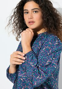 Multicolore blouse met een paarse basis en abstracte bloemenpatronen, elastische manchetten en een ronde halslijn. Zachte stof met een relaxte pasvorm.