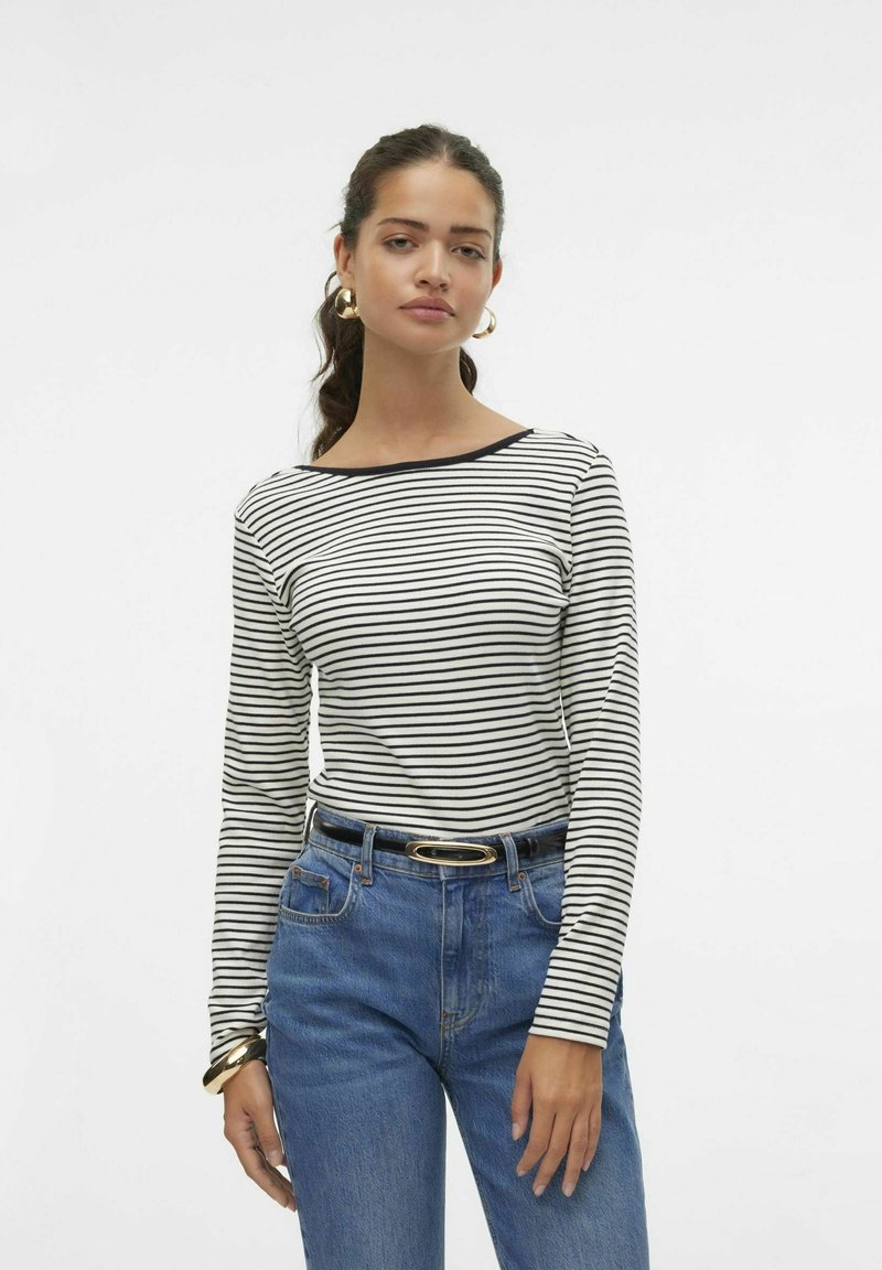 Gestreepte lange mouwen shirt in wit en zwart, met een bootneck. Gecombineerd met high-waisted blauwe denim jeans en een zwarte riem.