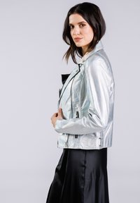 Veste de motard en cuir synthétique argenté métallisé avec des détails zippés classiques, un col à pression et une finition texturée, associée à une jupe en satin noire.
