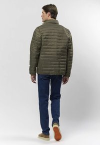 Jachetă matlasată kaki cu textură matlasată, guler înalt și fermoar. Asortată cu blugi albaștri și pantofi din piele întoarsă bej cu talpă de cauciuc.