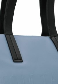 Borsa in pelle azzurro chiaro con manici neri, caratterizzata da testo impresso sul davanti e superficie liscia e opaca.