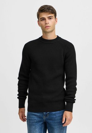 Black ribbed knit sweater with a crew neck, long sleeves, and ribbed cuffs, paired with blue jeans, against a plain light background.