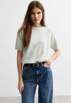 Lichtgrijze, korte mouwen gebreide trui gecombineerd met hoge taille blauwe jeans en een zwarte riem. Inclusief een gouden horloge om de pols.