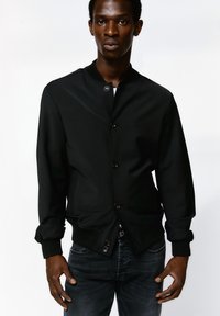 Schwarze Bomberjacke mit hohem Kragen, Knopfverschluss und gerippten Bündchen. Hergestellt aus einem glatten Material mit einer taillierten Passform.