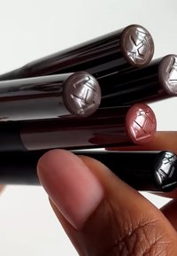 Fem læbestifter samlet, med glansfulde sorte hylstre med metalliske låg i nuancerne nude, brun, pink og bordeaux.