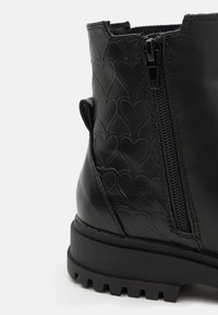 Černá kožená kotníková bota s texturou vzoru srdíček, boční zip a robustní podrážka. Hladký povrch a zaoblený design pro trvanlivost.