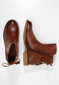 Bottes chelsea en cuir marron à bout rond, avec fermeture éclair sur le côté et lacets décoratifs. Semelle en caoutchouc épaisse avec un motif texturé pour une meilleure adhérence.
