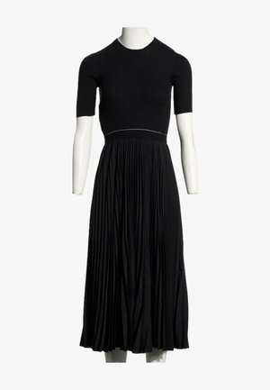 Robe midi noire avec haut ajusté à manches courtes côtelées et jupe fluide plissée, présentée sur un mannequin blanc sur fond blanc.
