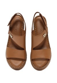 Sandalias de cuero marrón con diseño de talón abierto, que presentan cintas cruzadas anchas, detalles de costura y un cierre de hebilla. Textura suave.