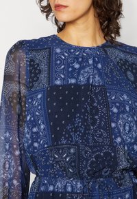Das navyfarbene Kleid ist mit einem Patchwork-Design ausgestattet, das aufwendige Paisley- und Blumenmotive enthält, und besteht aus einem leichten Stoff mit einer gerafften Taille.