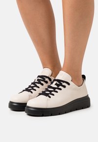 Cream leather sneakers with black laces and a black rubber sole. Rounded toe and cushioned heel for comfort.