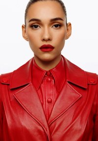Giacca di pelle rossa con colletto strutturato e bottoni frontali, abbinata a una camicia rossa a bottoni, entrambe con texture lisce.