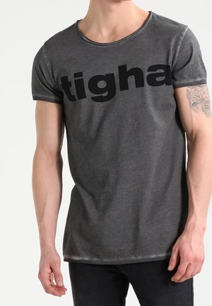 Camiseta de algodón gris con cuello redondo, mangas cortas y un gran logo negro impreso en el frente. Dobladillo ligeramente desgastado.