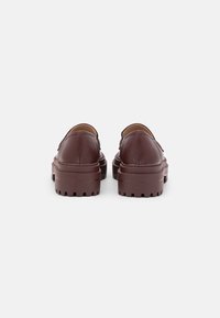 Zapatos de piel burdeos tipo slip-on con suela gruesa y con relieve, y punta redondeada; textura suave con un detalle de costura mínima.