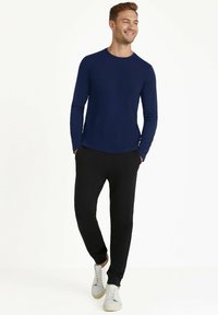 Marineblaue Langarmbluse kombiniert mit schwarzen Jogginghosen und weißen Sneakers, mit einem entspannten Schnitt und einem einfachen, klaren Design.