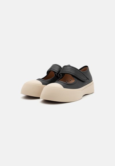 Sorte lædersko med rund tå og en beige gummisål. Har en velcro-rem og udskårne sider til ventilation.