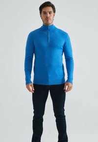 Pull bleu à manches longues avec col haut et zip quart. Fabriqué en tissu lisse, il présente une silhouette ajustée et des poignets côtelés.