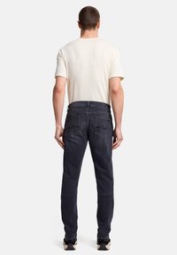 Mörka jeans för män i slim-fit med bakfickor och en slät textur, kombinerat med en ljusfärgad t-shirt med kort ärm.