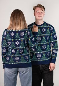 Knit Christmas sweaters featuring a navy background, white snowflakes, green trees, yellow stars, and colorful ornaments in a geometric pattern.