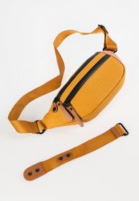 Borsa a vita gialla con parte superiore zippata nera, dettagli in pelle marrone e strap regolare. Presenta una superficie liscia e opaca e una forma arrotondata.