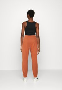 Camisola preta sem mangas com decote redondo, combinada com calças de jogging laranja. Textura suave, faixa elástica na cintura e design de perna estreita. Ténis visíveis.