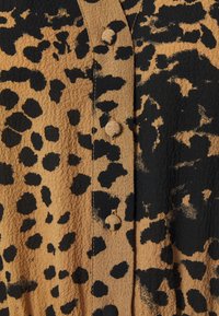 Tessuto in stampa leopardata, beige e nero, con una superficie texturizzata e bottoni rotondi lungo la chiusura.