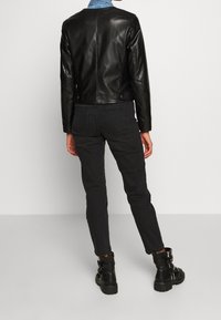Giubbotto di pelle nera con un design aderente, abbinato a jeans neri e stivaletti con fibbie metalliche. La vista posteriore mostra linee eleganti.