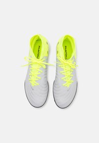 Zapatillas deportivas grises con superficie texturizada, que presentan cordones y detalles en amarillo brillante. El interior tiene un forro amarillo neón y se aprecia el logo.