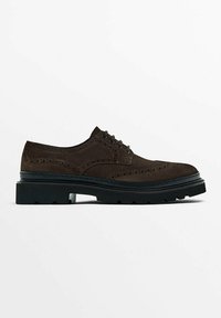 Chaussure brogue en daim marron foncé avec semelle noire épaisse et fermeture à lacets, présentant des perforations décoratives et un design à bout ailes.
