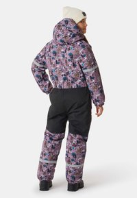 Paarse sneeuwpak met een bosdierenprint, zwarte accenten, reflecterende banden en een capuchon, gecombineerd met een witte gebreide muts.