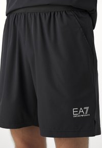 Čierne športové šortky vyrobené z ľahkej tkaniny, s elastickým pásom, bočnými vreckami a detailom bieleho loga EA7 Emporio Armani.