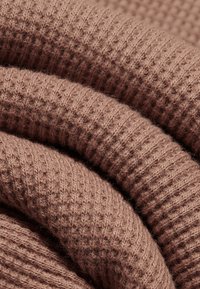 Tissu tricoté doux et plié avec une texture côtelée dans une couleur marron chaude et atténuée, montrant un fil fin et des coutures détaillées.
