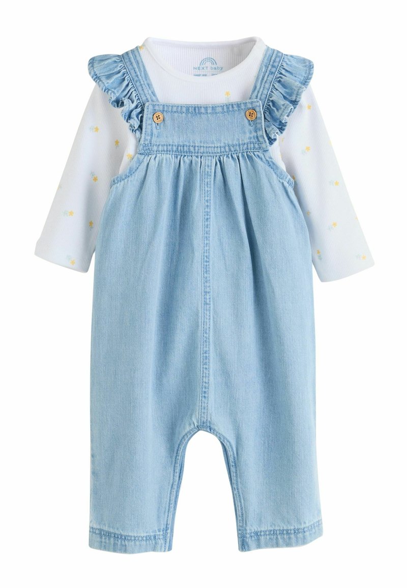 Ljusblå denimhänselbyxor med volangprydda axelband, träknappar och en vit långärmad tröja med pastellfärgade blommönster.