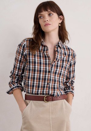Camicia button-up a quadri in navy, arancione e bianco. Tessuto in cotone con maniche arrotolate. Abbinata a una cintura marrone e pantaloni in corduroy beige.