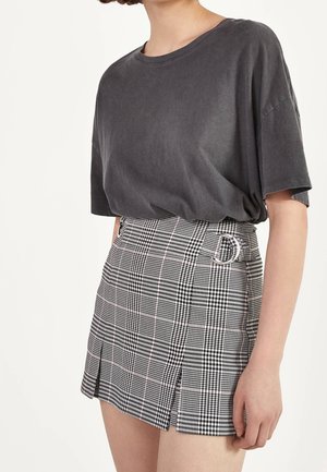 Kobieta nosząca luźny ciemnoszary t-shirt włożony do czarno-białej mini spódniczki w kratę z wysokim stanem, z pętlami na pasek i małymi rozcięciami.