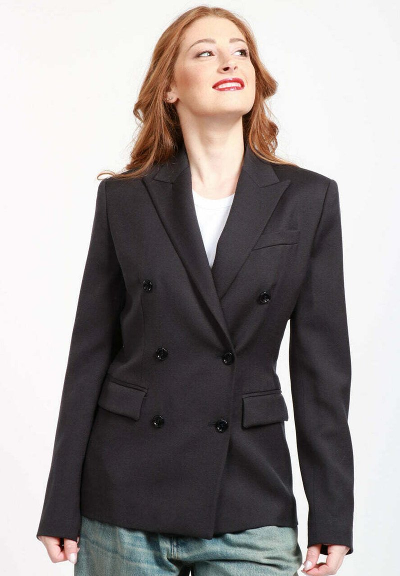 Blazer nero doppiopetto con risvolti, tasche con bottone e bottoni neri. Il tessuto è liscio con una vestibilità sartoriale.