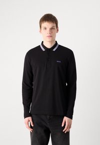 Polo preto de manga longa com uma pala de dois botões, apresentando um colarinho listrado em roxo e cinza e um pequeno logótipo roxo no peito.