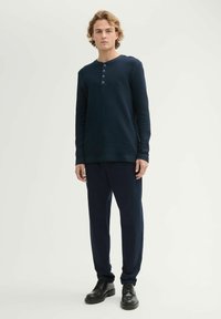 Granatowa, prążkowana bluzka z długim rękawem, z zapięciem na trzy guziki, w zestawieniu z dopasowanymi granatowymi spodniami i czarnymi sznurowanymi butami. Gładka faktura materiału.