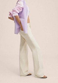 Leichte, weite Hosen aus Cremefarbe, kombiniert mit einem lavendelfarben gestreiften Hemd mit hochgekrempelten Ärmeln und legerer Passform.