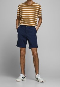 T-shirt a righe giallo senape e bianco abbinato a pantaloni corti blu con risvolto e sneakers bianche con accenti blu. Design dell'outfit semplice e casual.