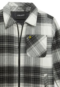 Zwart-witte geruite shirt gemaakt van stof met een ritssluiting aan de voorkant, een puntige kraag en een borstzak met een geel logo accent.