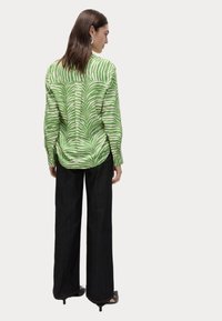 Groene en witte gestreepte blouse met lange mouwen, voorzien van een knoop achterop en een ontspannen pasvorm, gecombineerd met hoge zwarte wijde broek.