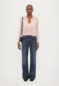 Lys rosa langermet skjorte med knapper, kombinert med vide mørkeblå denimjeans og svarte utsmykkede slip-on sko. En enkel, uformell antrekk.